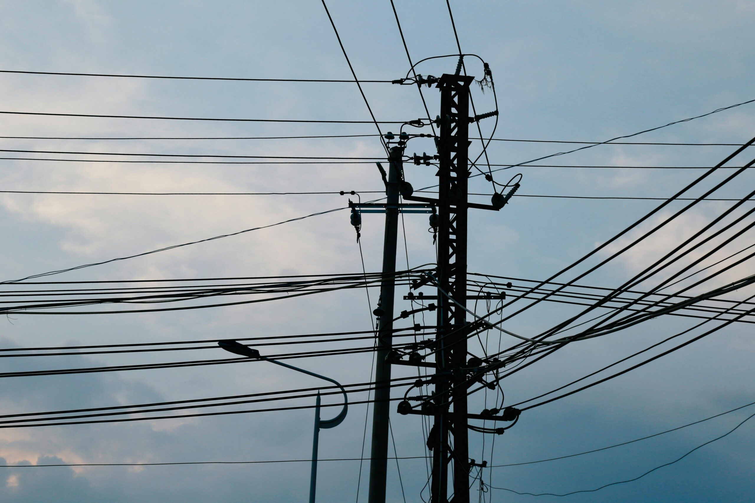 A complex network of power lines and pylons silhouetted against a bright sky.